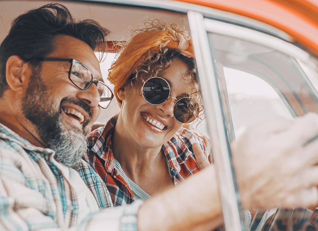 Read Our Reviews - Cheerful Middle Aged Couple Sitting in Their Car During a Road Trip While Looking at a Phone